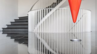 Ein roter Kegel hängt über einem glänzenden Boden, während eine geschwungene Treppe im Hintergrund sichtbar ist.