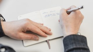 Eine Hand schreibt in ein Notizbuch, das den Titel "Meine Vision" und handschriftliche Notizen zeigt.