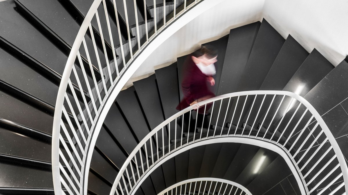 Eine Person in einem roten Kleid geht eine elegante, spiralförmige Treppe mit schwarzen Stufen hinunter.