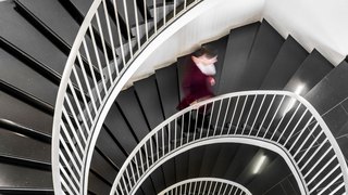 Eine Person in einem roten Kleid geht eine elegante, spiralförmige Treppe mit schwarzen Stufen hinunter.